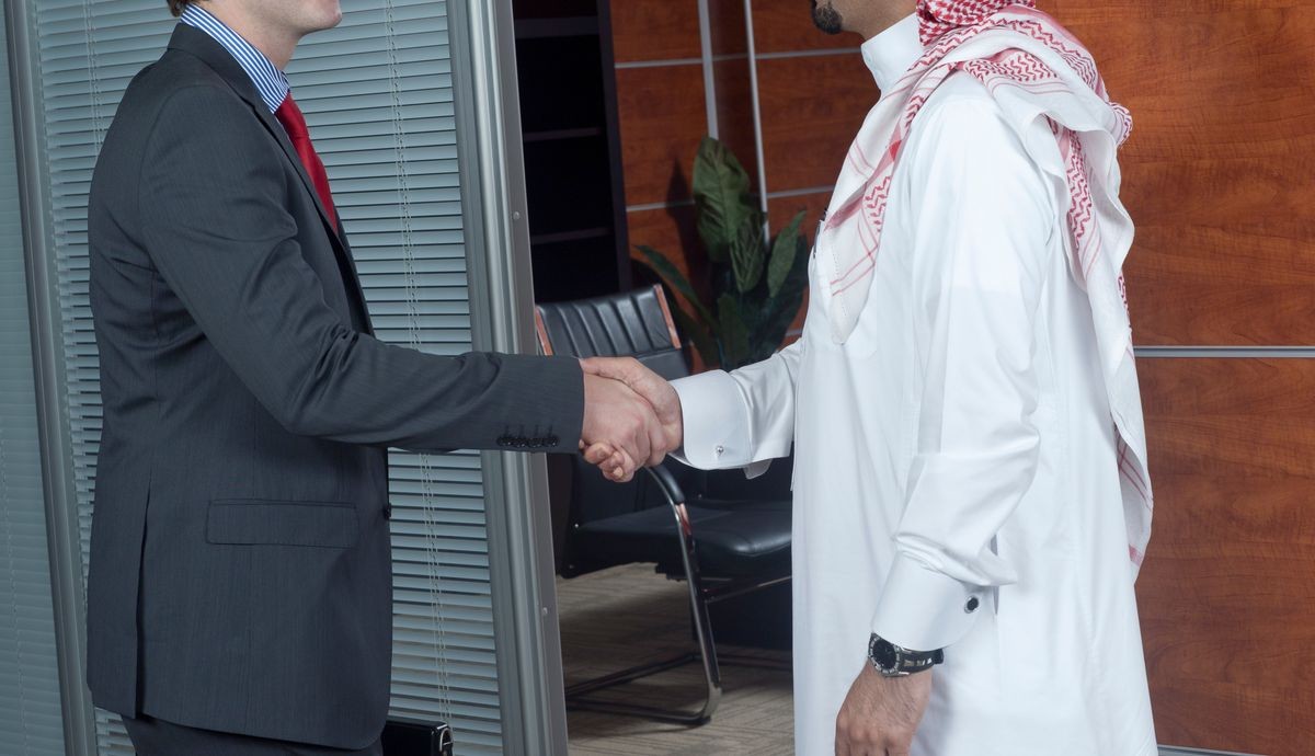 Middle eastern and caucasian businessmen shaking hands, in an office environment
